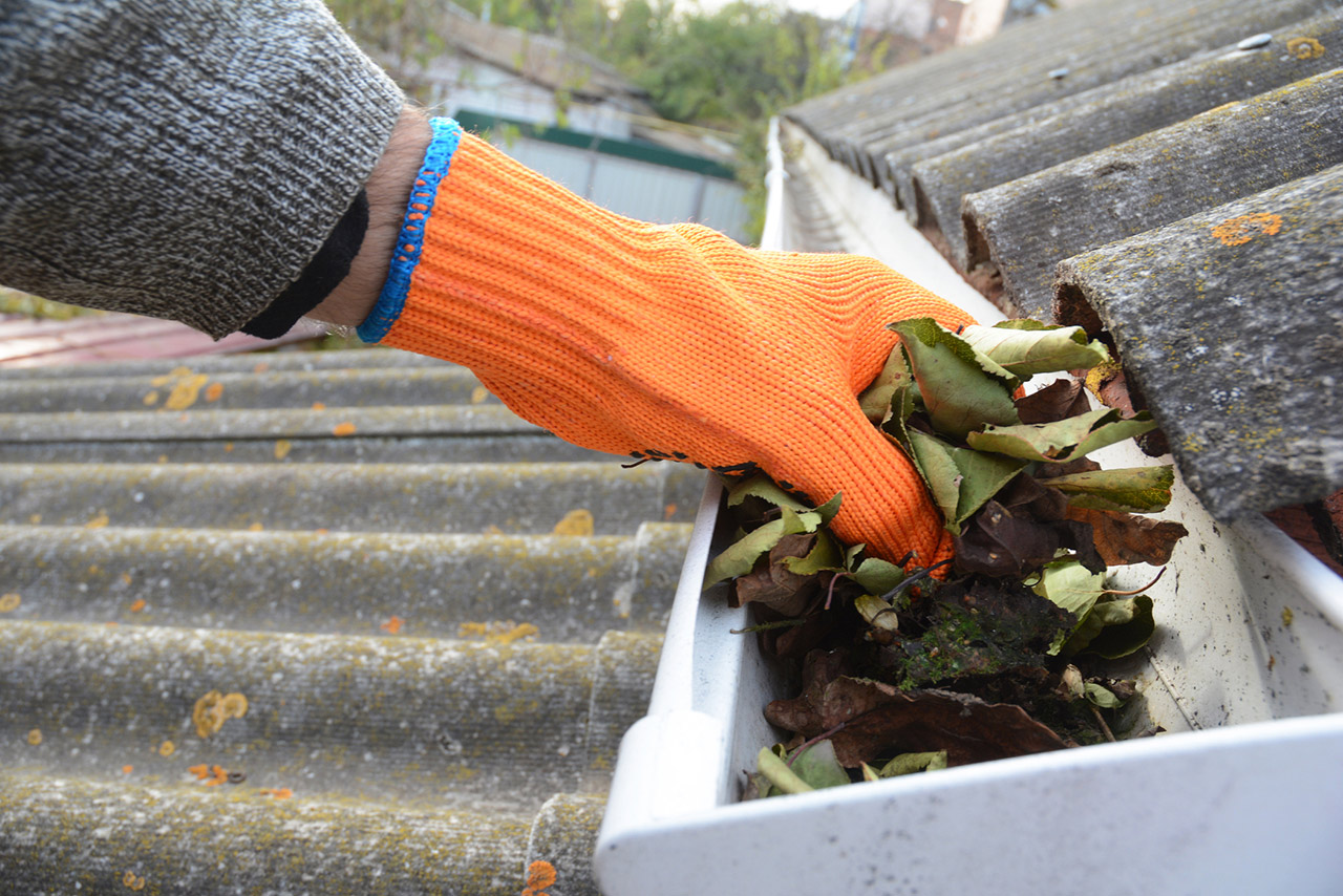 Roofer cleaning a rain gutter with an orange glove on