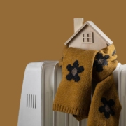 Wrapped in a warm scarf, a symbolic wooden house stands on an electric radiator