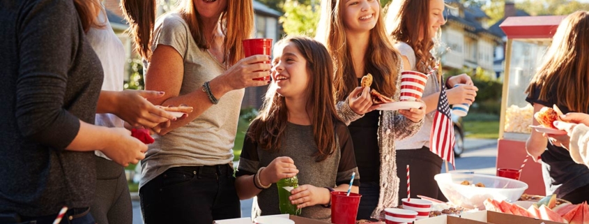 Girls stand talking at a block party food table, close up