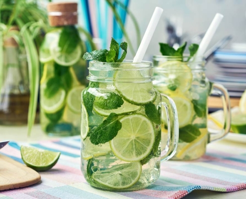 Two glasses and a bottle of homemade lemon, lime, and mint lemonade sit on the wooden dining table