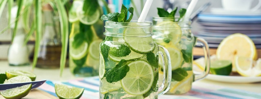 Two glasses and a bottle of homemade lemon, lime, and mint lemonade sit on the wooden dining table