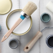 Paint brush, sponge roller, paints, waxes and other painting or decorating supplies on white wooden planks