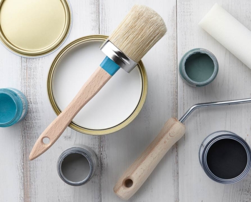 Paint brush, sponge roller, paints, waxes and other painting or decorating supplies on white wooden planks