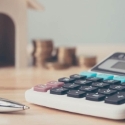 Calculator with wooden house and coins stack and pen on wood table