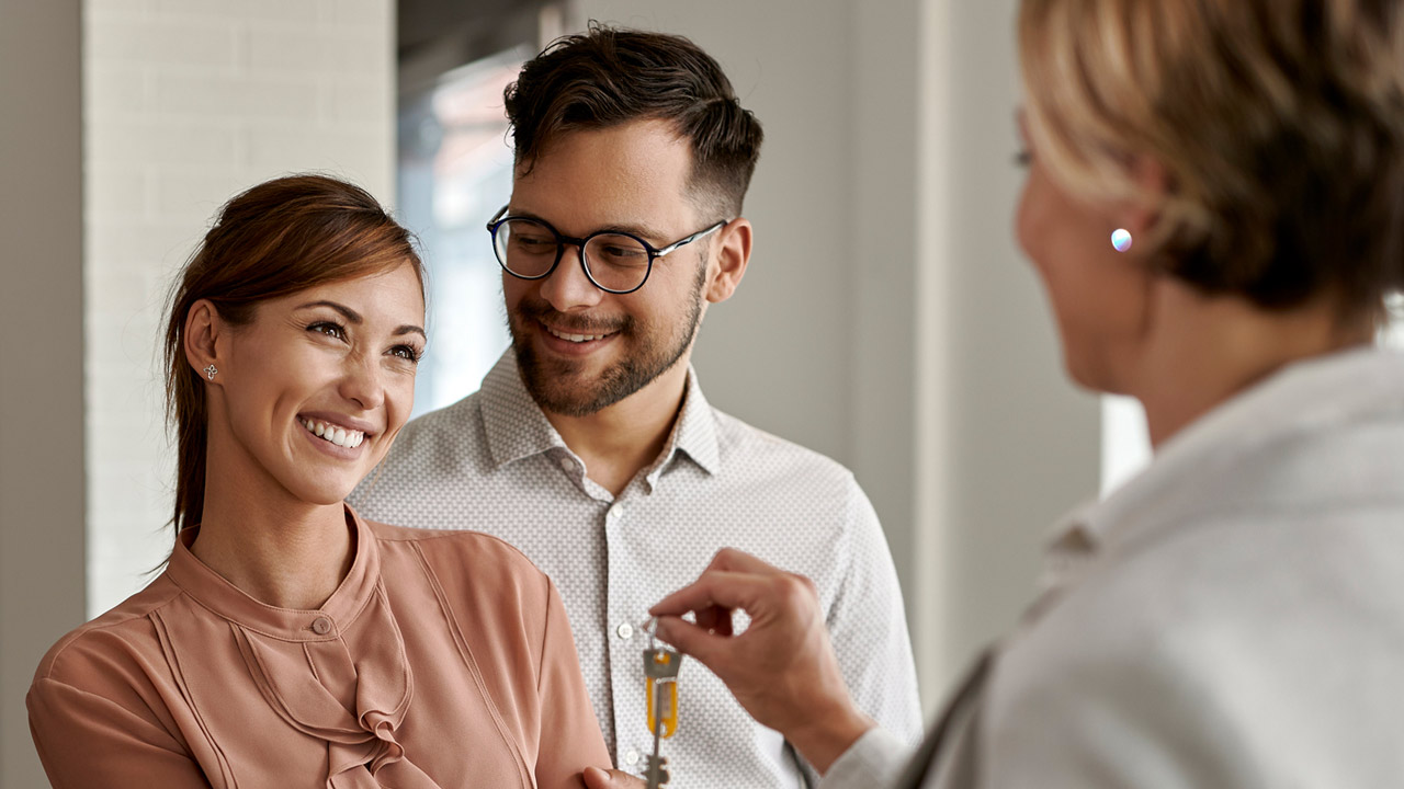 Happy couple buying new home and receiving house keys form real estate agent