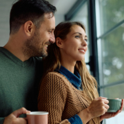 Smiling woman day dreaming while drinking coffee with her husband by the window at home