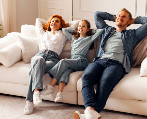 Cheerful family with child girl enjoying quality time at home in their living room, sitting on comfortable sofa, smiling and looking relaxed stock photo